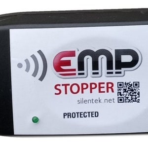 May include: Black rectangular device with a white label featuring the text "EMP STOPPER" in red and black. A green light is visible on the device. The label also includes a QR code and the website silentek.net.