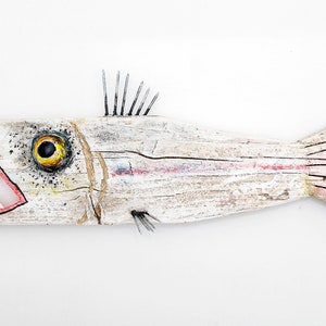 May include: A white wooden fish sculpture with a large open mouth, painted red with white teeth. The fish has a yellow eye with a black pupil and a black and white painted pattern on its body. The fish has a black painted fin and a white painted tail.