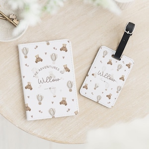 May include: A white passport holder and luggage tag set with a repeating pattern of teddy bears and hot air balloons. The text "The Adventures of Willow" is printed on the passport holder and "Willow" on the luggage tag.