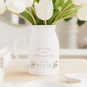 May include: A white ceramic pitcher with a handle, filled with white tulips. The pitcher has the text "Granny you're blooming lovely" and floral illustrations. The text "Love Isobel" is also included.