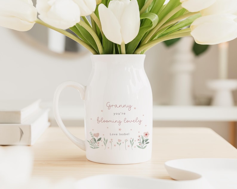 May include: A white ceramic pitcher with a handle, filled with white tulips. The pitcher has the text "Granny you're blooming lovely" and floral illustrations. The text "Love Isobel" is also included.
