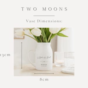 May include: A white ceramic vase with a handle, holding white tulips. The vase is 5.1 inches tall and 3.1 inches wide. It has the text "Sophie & Nick" and "Married 01.01.2020" printed on it. The words "TWO MOONS" are at the top.