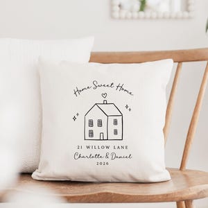 May include: Cream-colored decorative pillow with a black line drawing of a house, heart, and stars. Text reads "Home Sweet Home," "21 Willow Lane," and the names "Charlotte & Daniel" with the year "2026."
