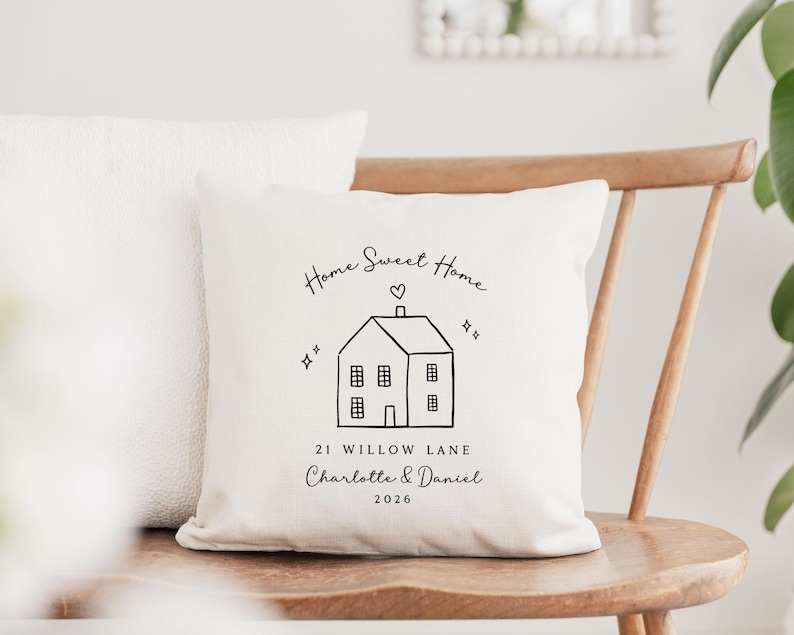May include: Cream-colored decorative pillow with a black line drawing of a house, heart, and stars. Text reads "Home Sweet Home," "21 Willow Lane," and the names "Charlotte & Daniel" with the year "2026."
