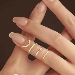 Peut inclure: Anneaux de doigt dorés en spirale. Les anneaux sont portés sur les doigts, avec un anneau en forme de croissant en haut et plusieurs bandes enroulées autour du doigt. Les anneaux sont sur une main avec des ongles manucurés.