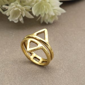 May include: A gold-coloured ring with a geometric design featuring two triangles. The ring has a double band and a polished finish. The ring is a piece of jewellery.