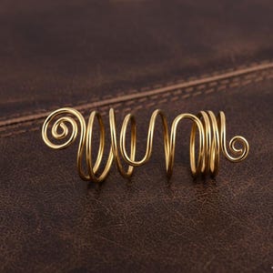 May include: A gold-colored hair accessory with a spiral design. The accessory is made of thin, curved metal and features a series of loops and swirls. The hair accessory is designed to be worn in the hair and adds a decorative element.