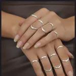 May include: A collection of ten thin, polished silver-toned rings worn on the fingers. Each ring features a simple, smooth band design with a subtle V-shaped or chevron-like curve, creating a uniform and metallic appearance across both hands.