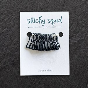 May include: A pack of black stitch markers with a white card that says "stitch squid knitting notions" and "stitch markers".