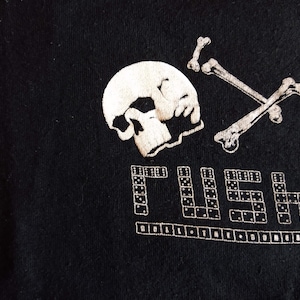 May include: Black t-shirt with a white skull and crossbones design. The text "RUSH" is written in white below the skull and crossbones. The text "ROLL THE DICE" is written in white below the word "RUSH".