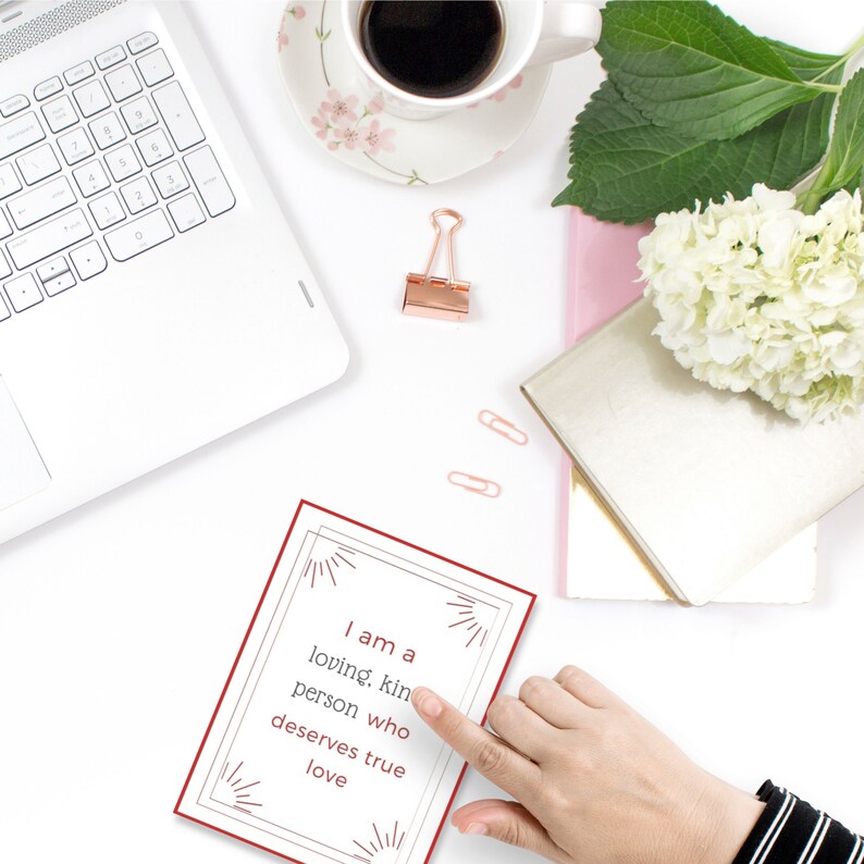 Puede incluir: Una tarjeta roja con un borde blanco y texto blanco que dice "Soy una persona cari&ntilde;osa y amable que merece un amor verdadero". El texto est&aacute; rodeado por un dise&ntilde;o decorativo de l&iacute;neas radiantes.