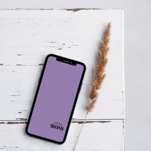 May include: A black smartphone with a lavender screen displaying the words "Keep Going" in a handwritten font. The phone rests on a distressed white wooden surface, accompanied by a dried, tan-colored plant stem.