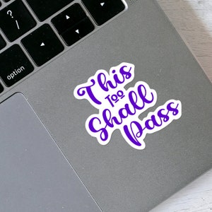 May include: Purple vinyl sticker with the text "This Too Shall Pass" on a silver laptop.
