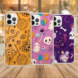 May include: Three clear phone cases with Halloween-themed designs. The first case has a yellow, orange, and white design with candy, stars, and a ghost. The second case has a purple, white, and black design with candy, stars, and a ghost. The third case has a purple, white, and black design with a bat, a potion bottle, and stars.