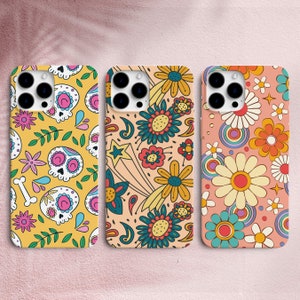 May include: Three phone cases with different designs. The first case has a yellow background with a skull and flower pattern. The second case has a pink background with a flower and star pattern. The third case has a light blue background with a flower and circle pattern.