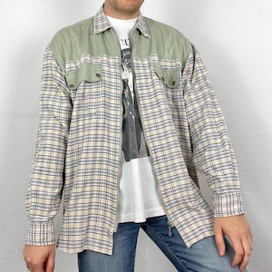 Può includere: Una camicia a maniche lunghe a quadri beige e blu con un inserto in velluto a coste verde e chiusura a zip.