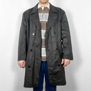 May include: A long black leather coat with a double breasted closure and a collar. The coat has two pockets on the front and a belt in the back.