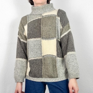 Könnte beinhalten: Ein grauer, brauner und weißer Pullover mit Rollkragen. Der Pullover hat ein kariertes Muster mit einem hohen Kragen.