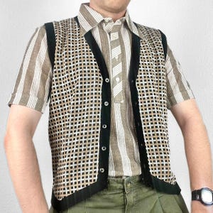 May include: A retro outfit comprising a striped shirt, a patterned vest, and olive green trousers. The vest has a black trim and a grid pattern in black, white, and tan. A black watch is visible on the wrist.