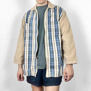 Può includere: Giacca con zip, colletto e maniche in velluto a coste. Il davanti presenta un motivo a quadri blu e bianco con strisce verticali. La giacca è aperta, rivelando una maglietta grigia. Le maniche e il colletto sono beige.