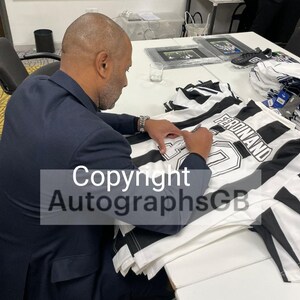 May include: A person signing a white and black striped soccer jersey with the name "Ferdinand" printed on the back.