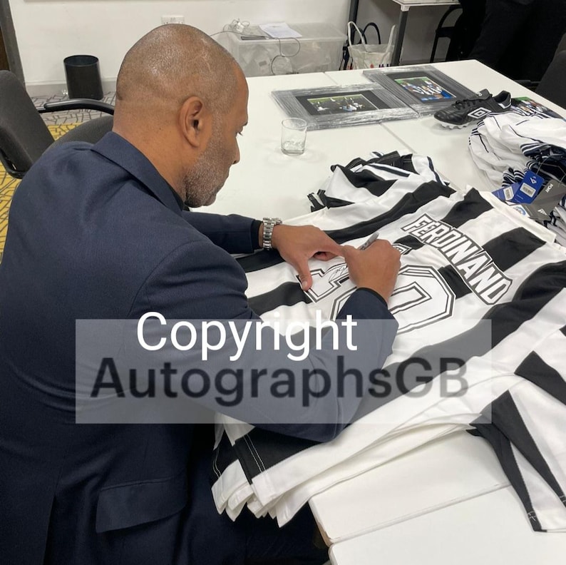 May include: A person signing a white and black striped soccer jersey with the name "Ferdinand" printed on the back.
