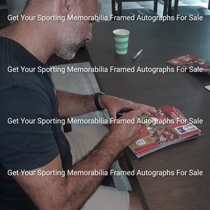 May include: A person signing a 1999 FA Cup semi-final replay program. The program is red and white with a picture of a soccer game. The text "Get Your Sporting Memorabilia Framed Autographs For Sale" is repeated on the image.