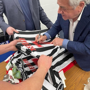 Może przedstawiać: Osoba podpisująca czarno-białą, pasiastą koszulkę piłkarską z czerwonym napisem "Wigan Athletic".