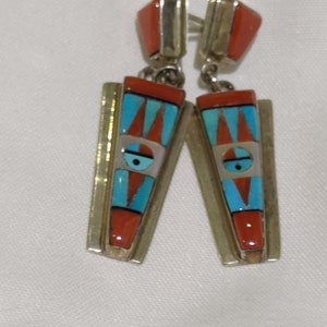 Op de afbeelding: Een paar oorhangers met een geometrisch ontwerp. De oorhangers zijn gemaakt van zilver en hebben turquoise, koraal en parelmoer inlegwerk.