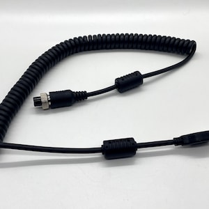 Può includere: Un cavo nero a spirale con un connettore USB su un'estremità e un connettore circolare sull'altra estremità.