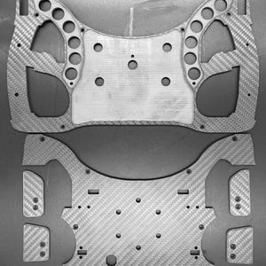 Op de afbeelding: Twee zwarte koolstofvezelplaten met meerdere gaten en een rasterpatroon. De platen zijn ontworpen om samen te worden gebruikt om een frame of structuur te creëren.