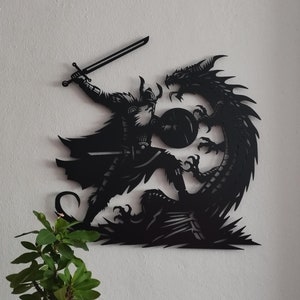 May include: Black metal wall art depicting a Viking warrior battling a dragon. The warrior is holding a sword and shield, while the dragon is attacking with its claws and teeth.