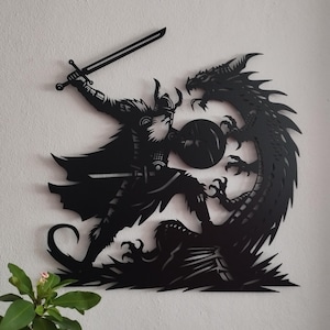 May include: Black metal wall art depicting a warrior with a sword and shield fighting a dragon. The warrior is wearing a helmet and armor. The dragon is curled around the warrior's legs.