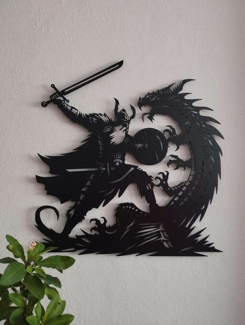 May include: Black metal wall art depicting a warrior with a sword and shield fighting a dragon. The warrior is wearing a helmet and armor. The dragon is curled around the warrior's legs.