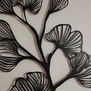 May include: Black metal wall art featuring a stylized ginkgo branch with multiple fan-shaped leaves. The leaves have detailed linear patterns, and the artwork is mounted on a textured white wall. This decorative piece adds a touch of nature-inspired elegance.