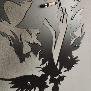 K&ouml;nnte beinhalten: Ein Wandkunstobjekt aus mattschwarzem Metall mit einer lasergeschnittenen Silhouette eines Raben oder einer Kr&auml;he mit detaillierter Federzeichnung. Auf der R&uuml;ckseite befindet sich eine kleine, metallene Zackenaufh&auml;ngung.