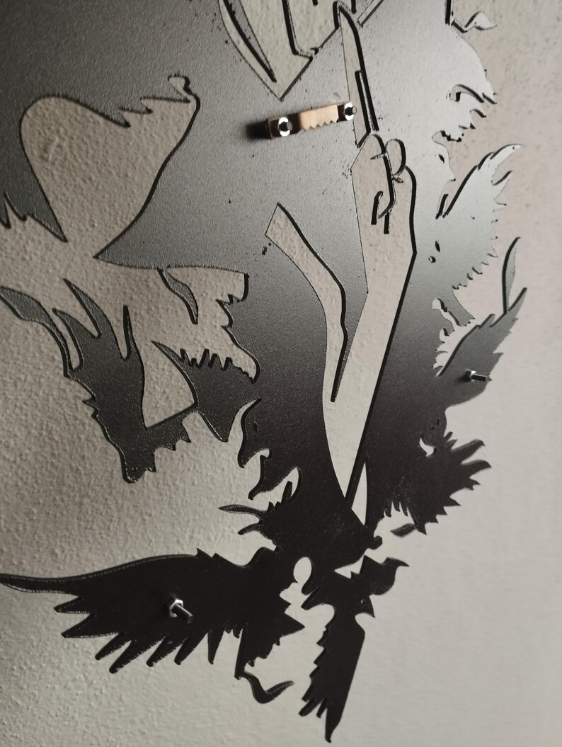 K&ouml;nnte beinhalten: Ein Wandkunstobjekt aus mattschwarzem Metall mit einer lasergeschnittenen Silhouette eines Raben oder einer Kr&auml;he mit detaillierter Federzeichnung. Auf der R&uuml;ckseite befindet sich eine kleine, metallene Zackenaufh&auml;ngung.