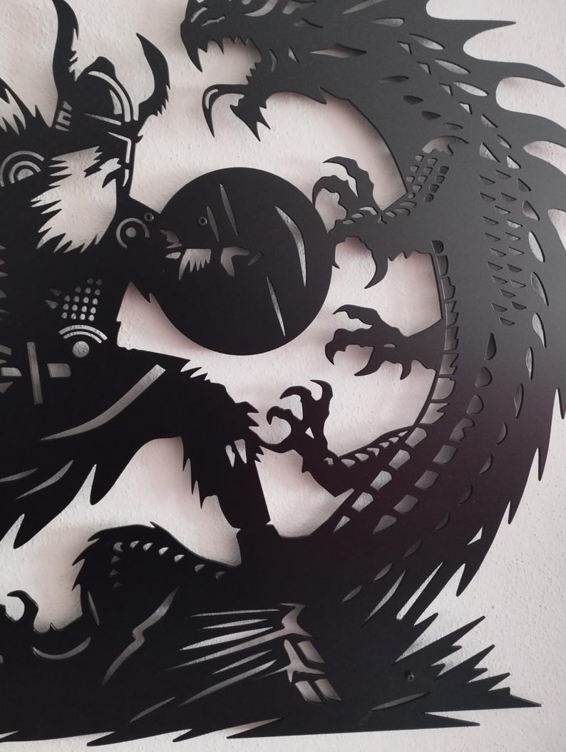 May include: Black metal wall art depicting a Viking warrior with a shield facing a dragon. The warrior is holding a sword and the dragon is in a defensive posture.