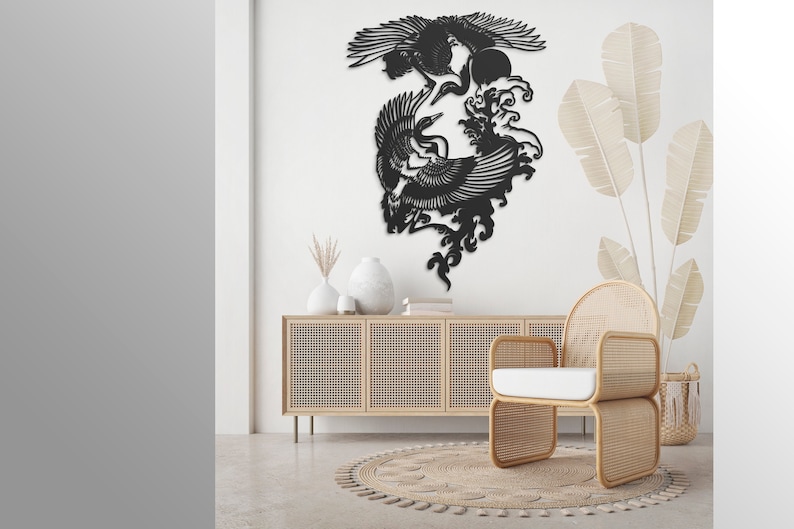 K&ouml;nnte beinhalten: Ein schwarzes Wandkunstobjekt aus Metall mit einem detaillierten Scherenschnitt-Design von zwei fliegenden Kranichen, platziert &uuml;ber stilisierten Wellen und einer kreisf&ouml;rmigen Sonne. Die komplexe Silhouette zeigt die V&ouml;gel mit ausgebreiteten Fl&uuml;geln.
