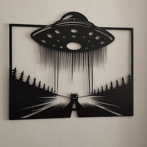 Könnte beinhalten: Schwarze Wandkunst aus Metall, die ein UFO darstellt, das über einer Straße mit Bäumen auf beiden Seiten schwebt. Das UFO sendet Lichtstrahlen auf die Straße.