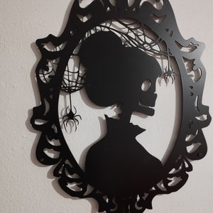 Pode incluir: Decora&ccedil;&atilde;o de parede de metal preto com uma silhueta de um esqueleto em uma moldura com teias de aranha e aranhas.