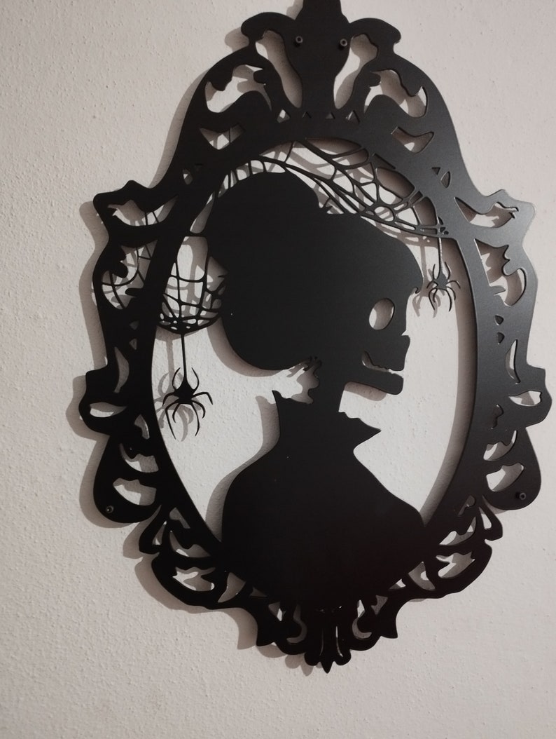 Pode incluir: Decora&ccedil;&atilde;o de parede de metal preto com uma silhueta de um esqueleto em uma moldura com teias de aranha e aranhas.