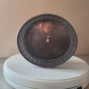 May include: A silver cake stand with a decorative, openwork border. The stand has a circular base and a flat top.