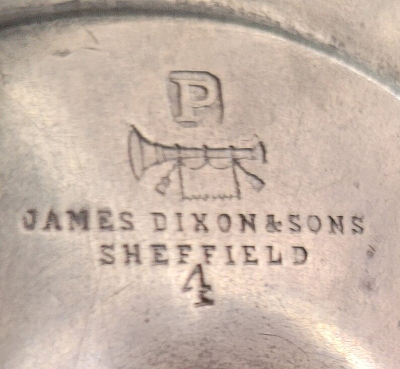May include: Close-up of a silver mark with the letter "P" above a stylized trumpet with a banner and the text "JAMES DIXON & SONS SHEFFIELD 4".