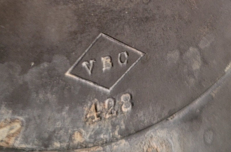 May include: Close-up of a black metal object with a diamond-shaped mark that says "VBC" and the number "428" below it.