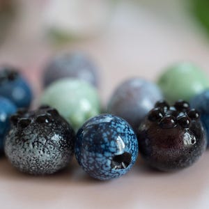 May include: A collection of blue, green, and black glass beads with speckled patterns. The beads are round and have a glossy finish.