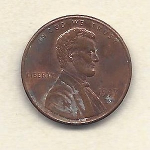 May include: A close-up of a copper-coloured penny. The coin features a profile of Abraham Lincoln, with the words "IN GOD WE TRUST" and "LIBERTY" visible. The year "1927" is also displayed on the coin.