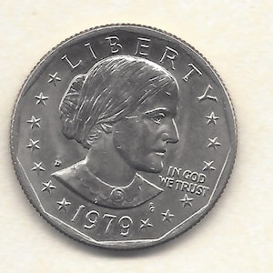 Pode incluir: Uma moeda prateada com o perfil de uma mulher, a palavra "LIBERTY" no topo e o ano "1979" na parte inferior. A frase "IN GOD WE TRUST" também está visível.
