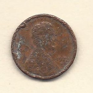 May include: A well-used copper penny from 1972, featuring a man's profile. The coin shows signs of wear and tear, with some areas discoloured. The date "1972" is partially visible on the right side of the coin.
