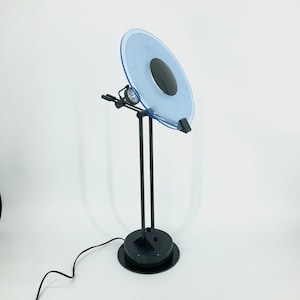 May include: A black and blue desk lamp with a round, translucent blue shade and a black base. The lamp has a single light bulb and a black arm that extends from the base to the shade.
